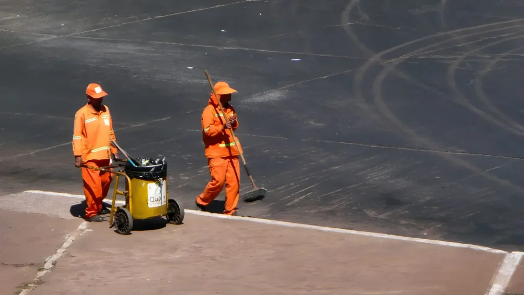 Dois garis de uniforme laranja varrendo uma via pública