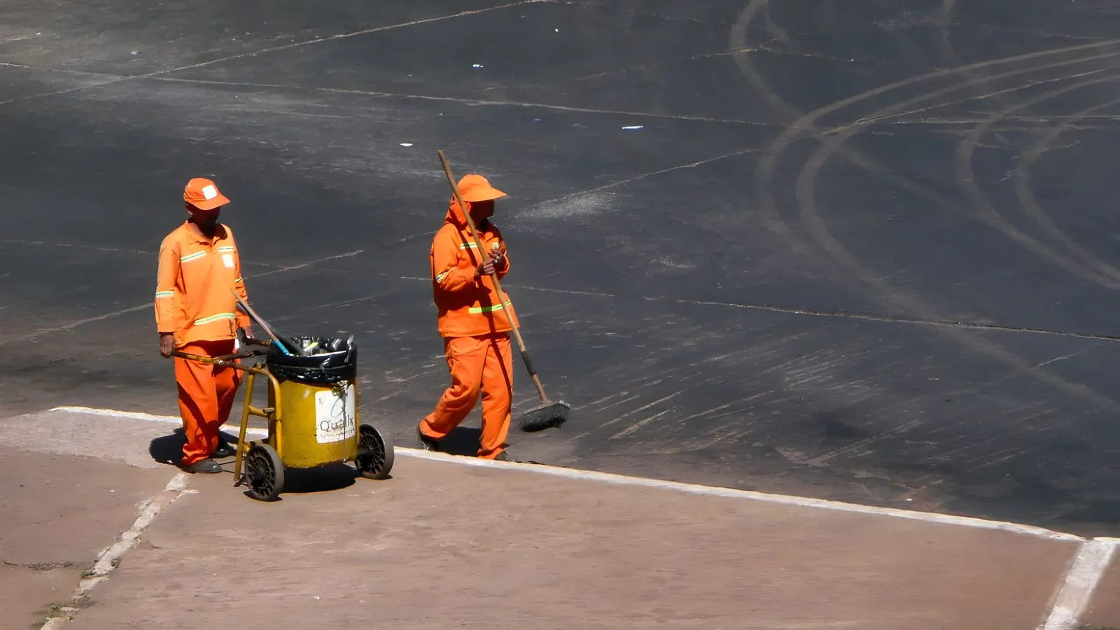 Dois garis de uniforme laranja varrendo uma via pública